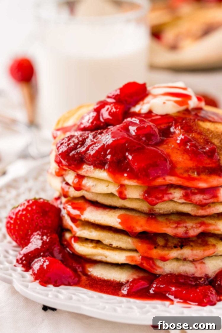 Close up photo of a stack of strawberry pancake covered in strawberry sauce.