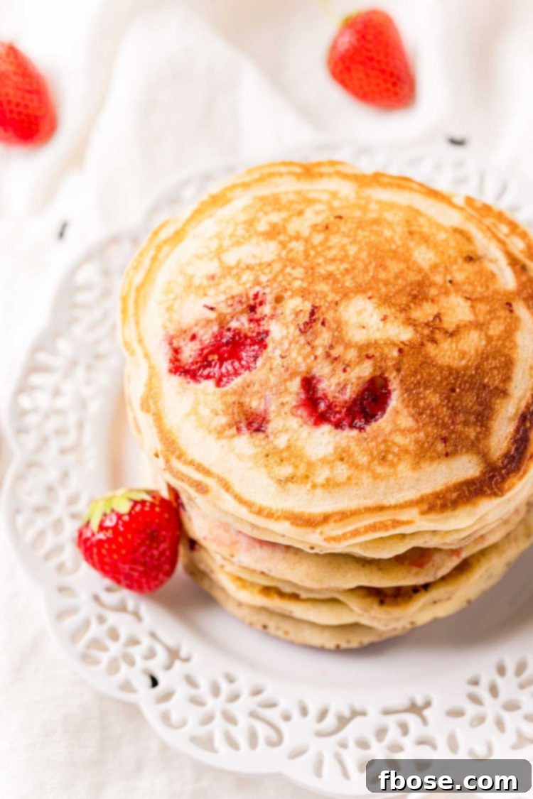 A stack of strawberry pancakes on a white plate.