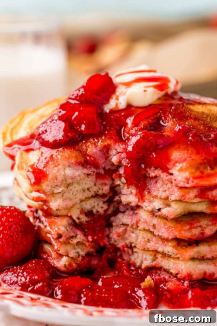 A stack of strawberry pancakes covered in strawberry sauce with a bite taken out of it.