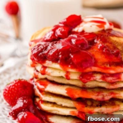 Close up photo of a stack of strawberry pancake covered in strawberry sauce.