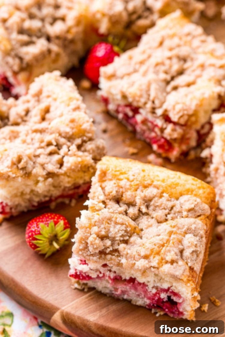 Slices of coffee cake on a wooden cutting board with strawberries scattered around.