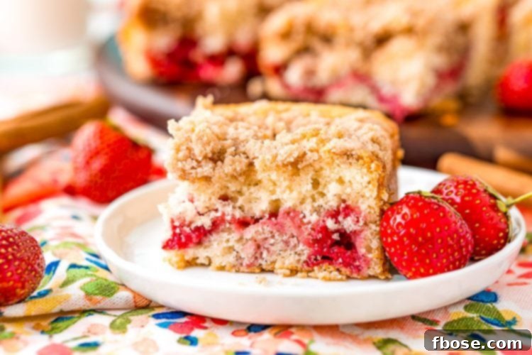 Strawberry coffee cake slice sitting on a white dessert plate with more strawberries scattered around.