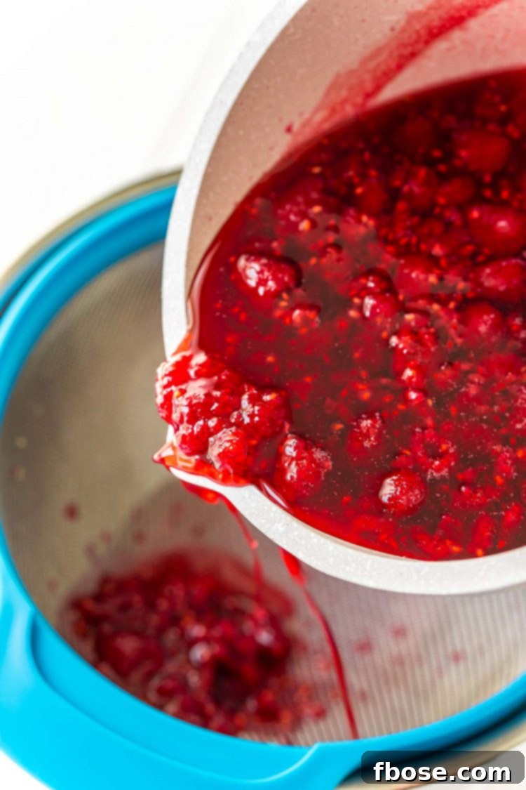 Ruby Raspberry Elixir 5 Raspberries being run through a fine mesh strainer to make simple syrup.