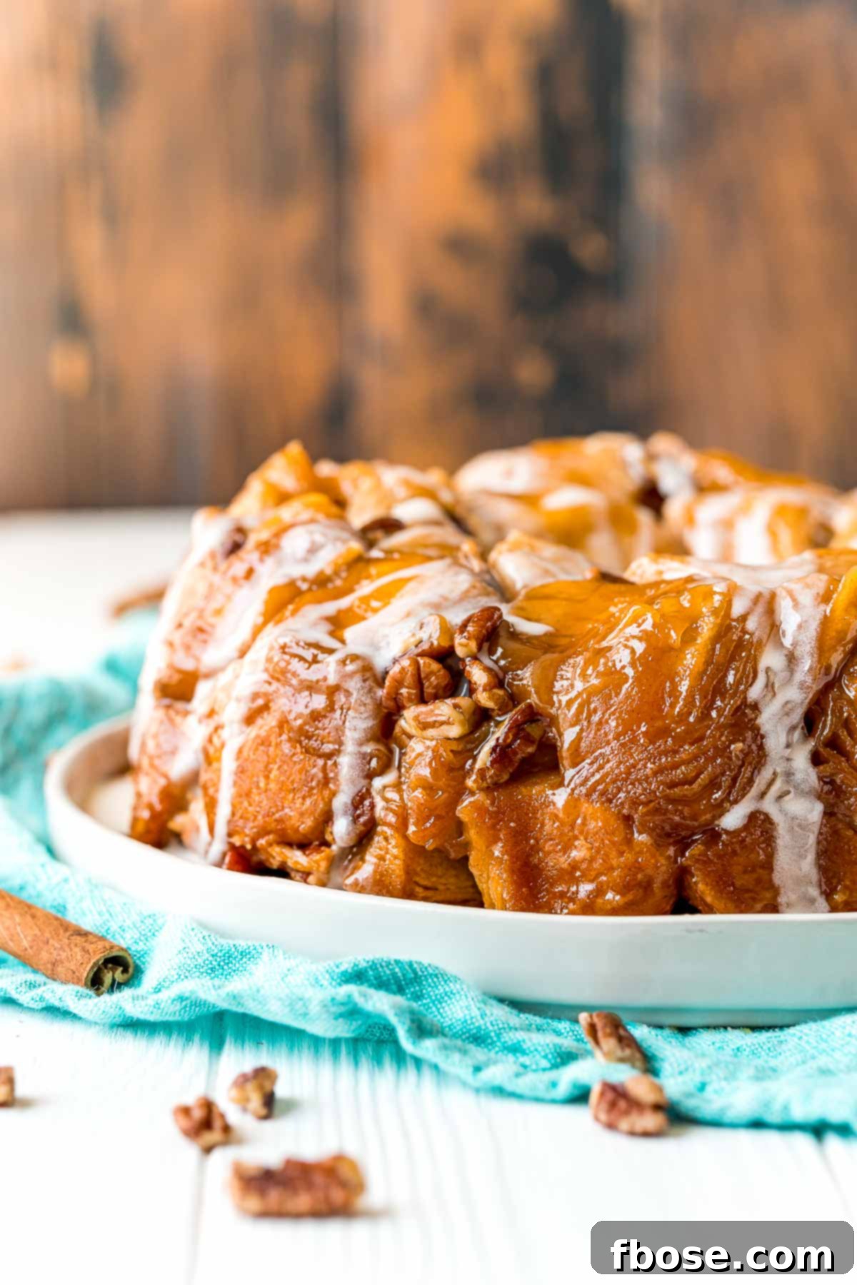 Monkey bread on a white plate on a teal napkin with pecans scattered around.