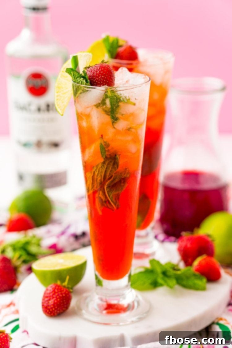Two tall glasses of vibrant red Strawberry Mojitos garnished with fresh mint and strawberries, set against a summer backdrop.