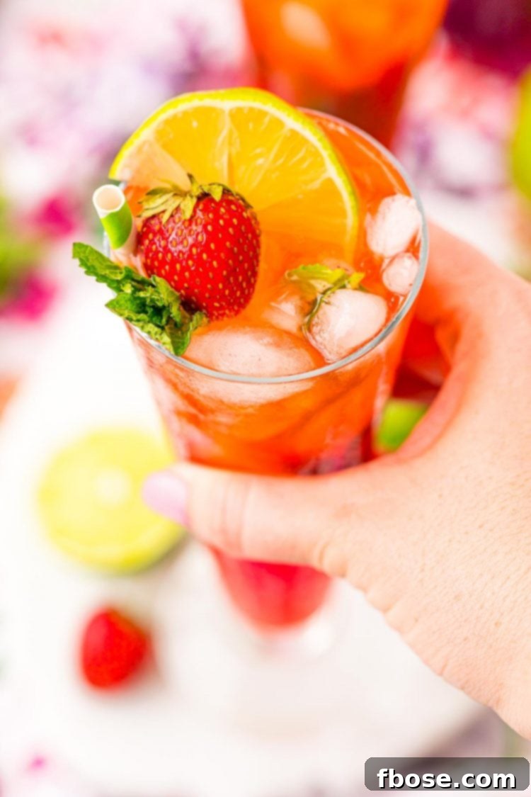 A close-up of a woman's hand holding a beautifully garnished Strawberry Mojito in a tall glass, showcasing the drink's vibrant color and refreshing appeal.