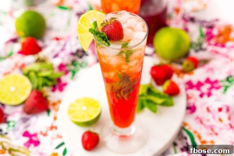 A wide-angle shot of a vibrant strawberry mojito cocktail in a tall glass, garnished with fresh mint and lime slices, invitingly placed on a wooden surface.