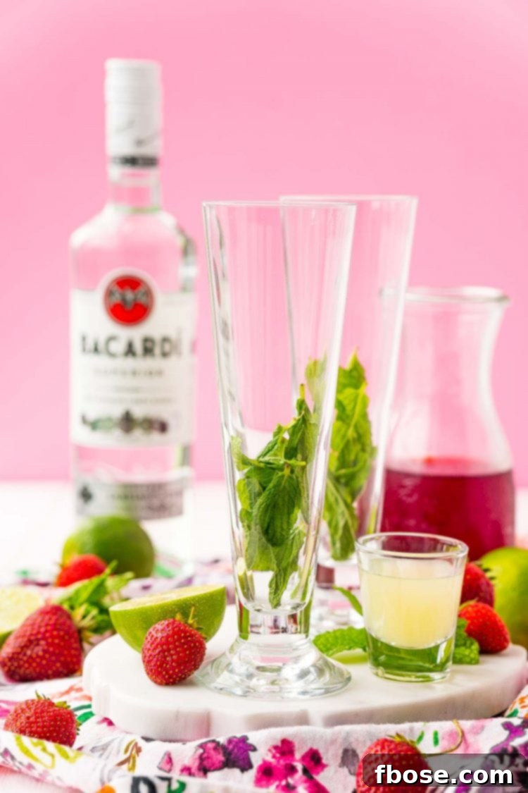 Fresh mint leaves arranged at the bottom of a tall cocktail glass, with a blurred bottle of rum in the background, signaling the start of cocktail preparation.