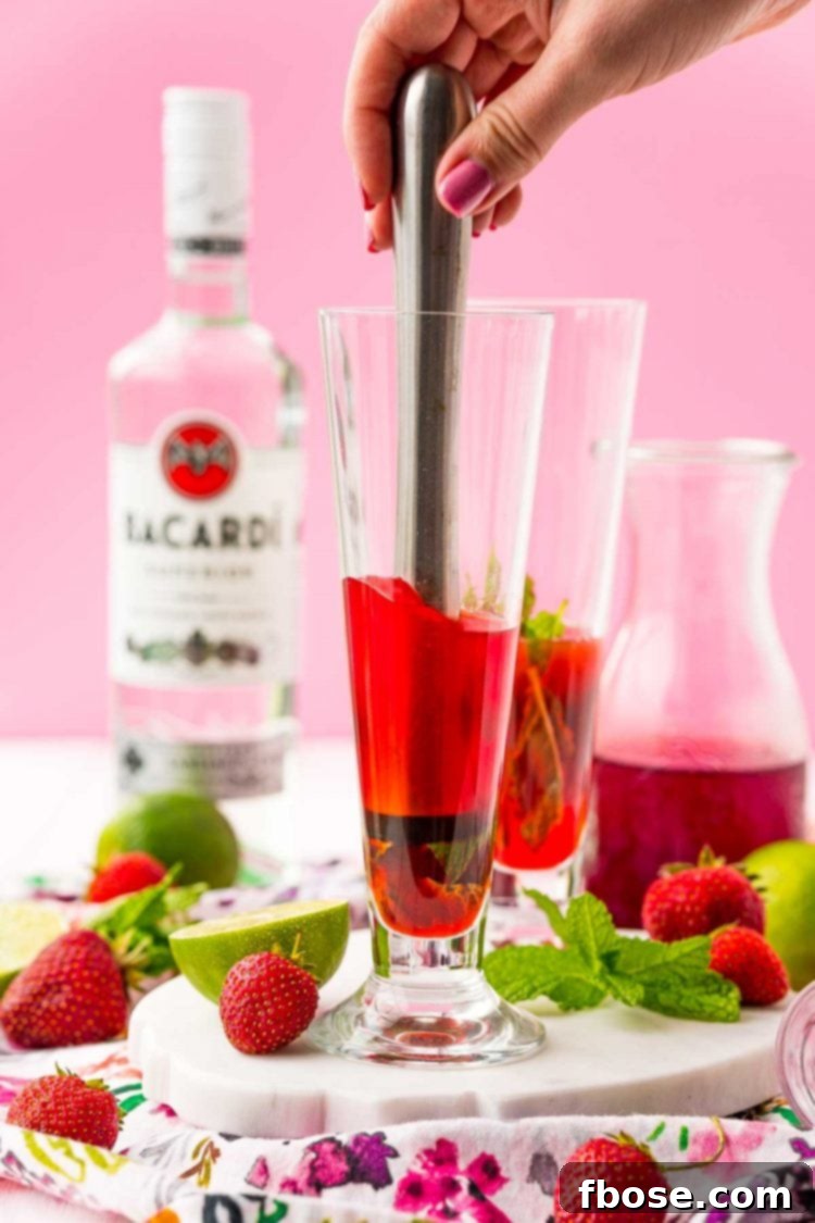 A bartender's muddler being used to gently press and twist the ingredients in a cocktail glass, creating the base for a mojito.