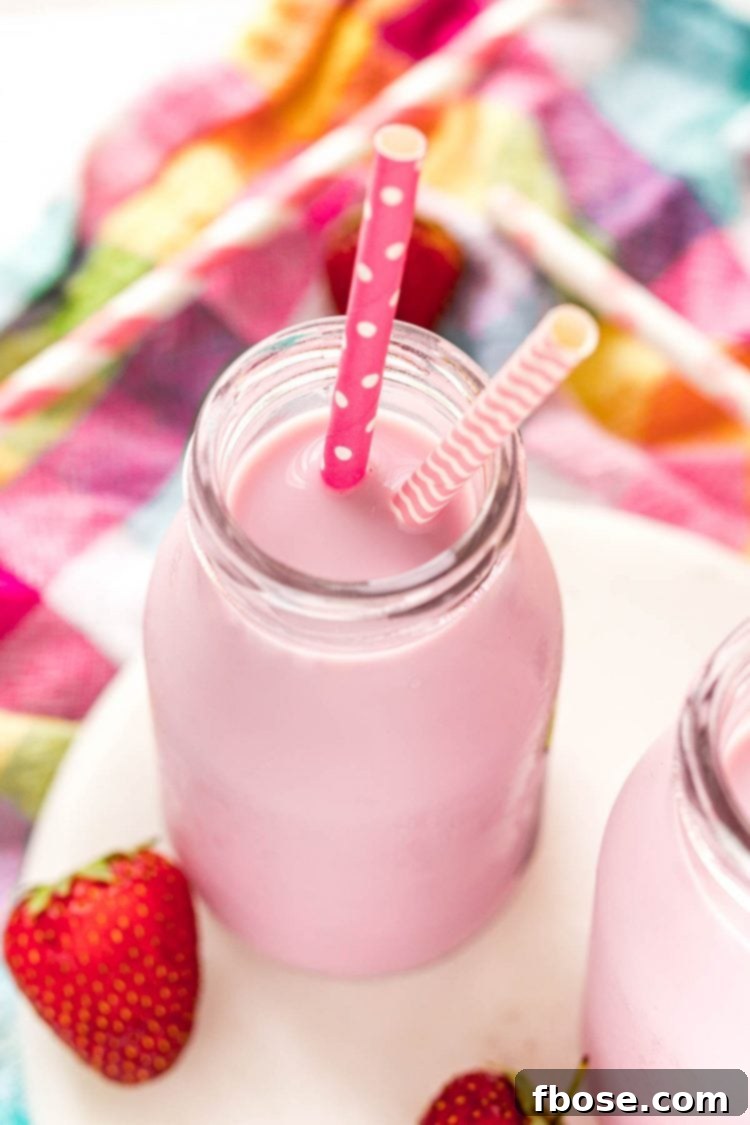 Close up photo of a milk bottle with strawberry milk in it on a white marble board on a colored checkered napkin.