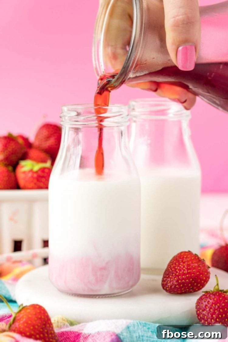 Strawberry simple syrup being poured into a bottle of milk.