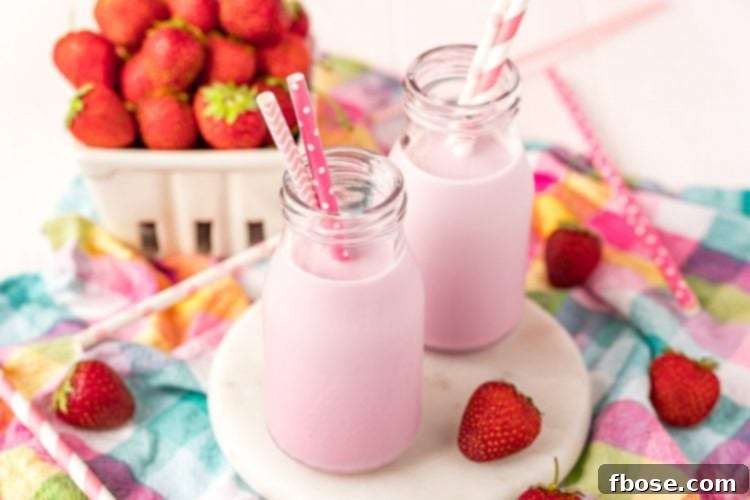 Close up horizontal photo of two milk bottles with strawberry milk and pink straws in them on a white board on a colorful napkin.