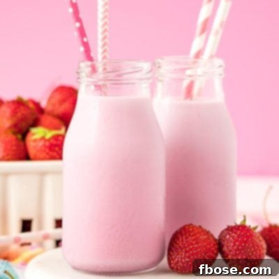 Close up photo of two milk bottles of homemade strawberry milk on a white board.