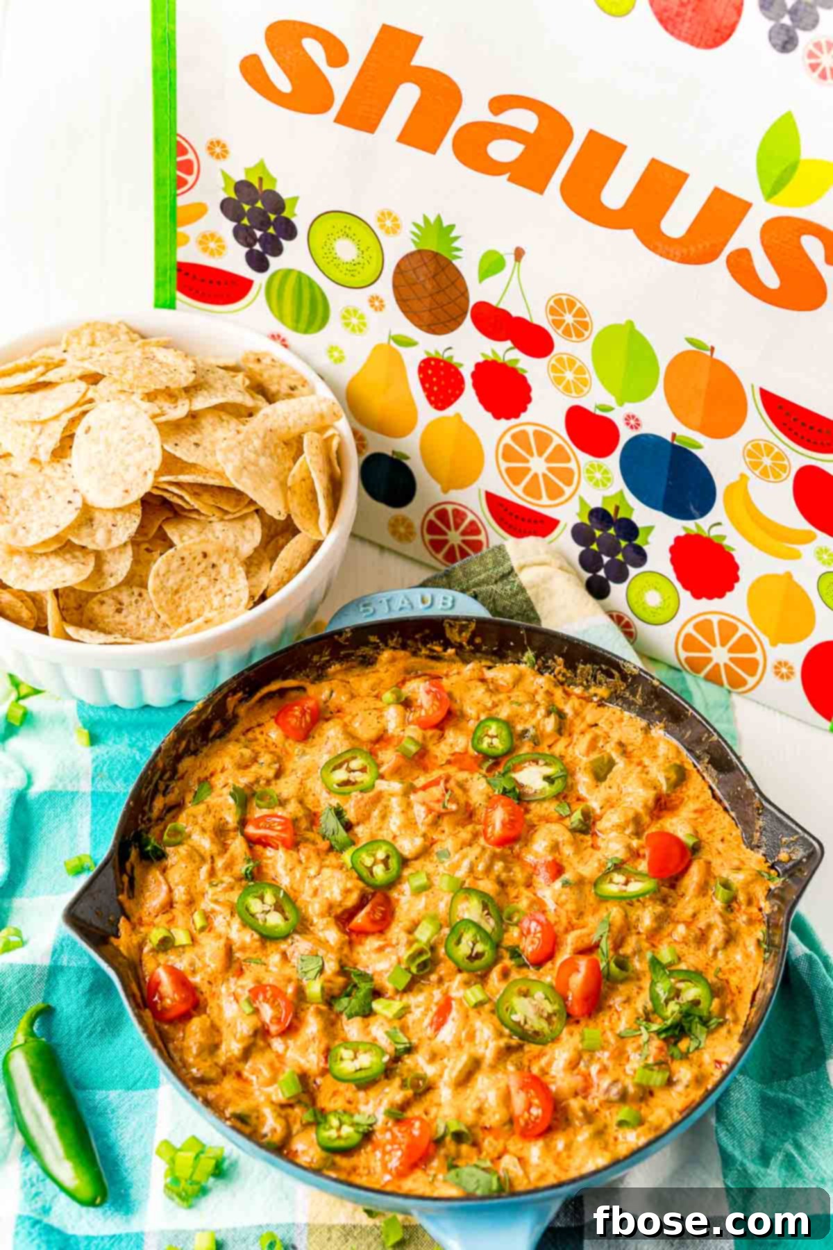A close-up of a cast-iron pan overflowing with golden-brown cheesy sausage dip, served with a basket of crunchy tortilla chips.