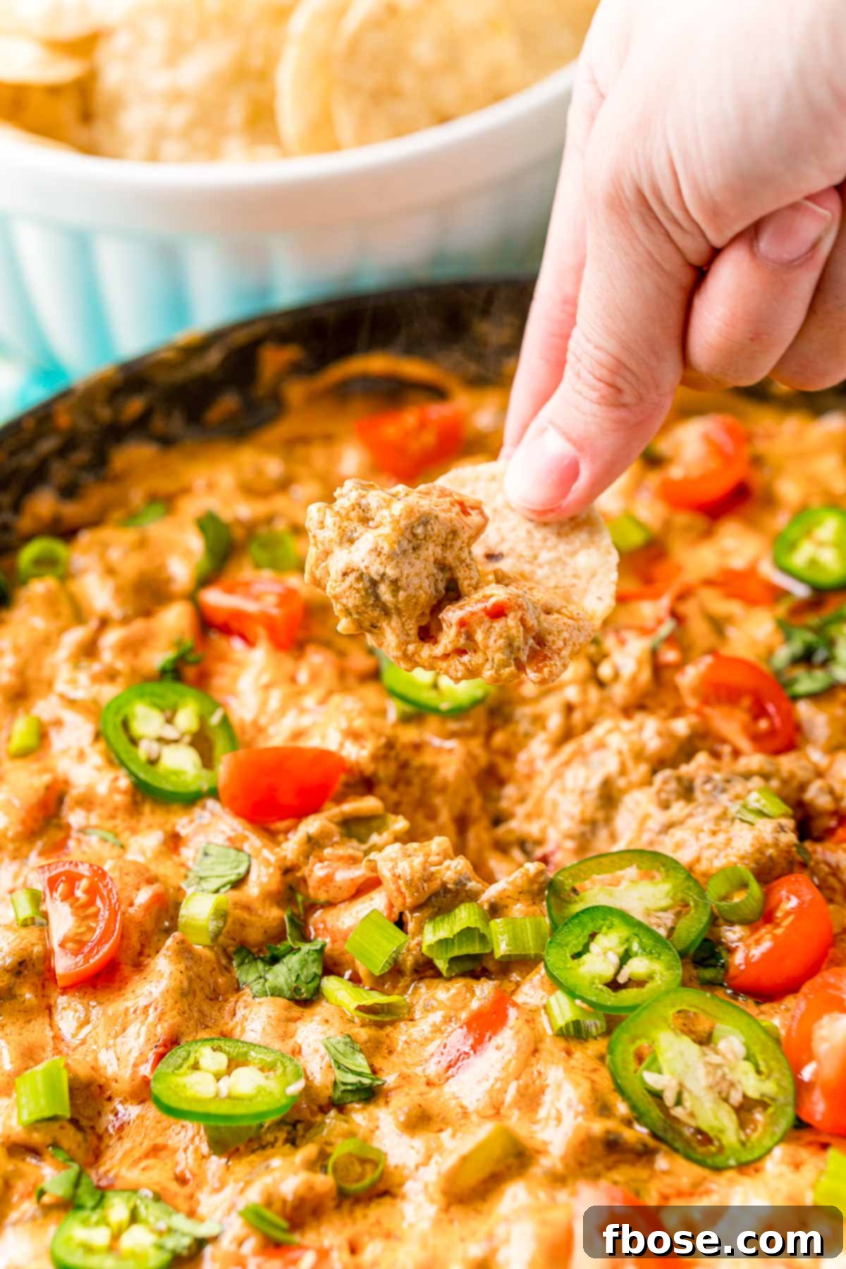 A hand dipping a tortilla chip into a bowl of creamy Cheesy Sausage Dip, highlighting its rich texture.