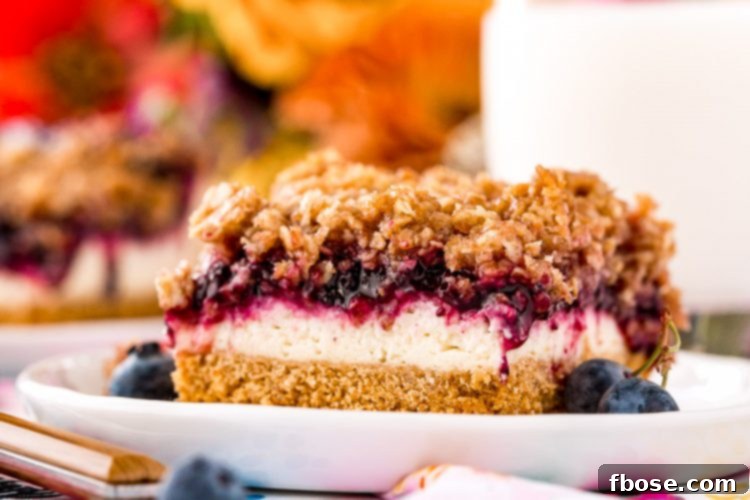 Ultimate Blueberry Cheesecake Bars 3 Slice of blueberry cheesecake with crumble topping on a white plate.