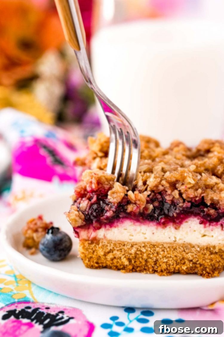 Ultimate Blueberry Cheesecake Bars 9 Fork taking a bite out of a slice of blueberry cheesecake with crumb topping.