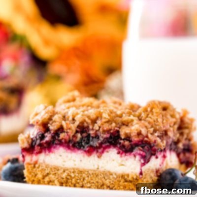 Ultimate Blueberry Cheesecake Bars 10 Close up photo of a slice of blueberry cheesecake bars on a white plate with milk and sunflowers in the background.
