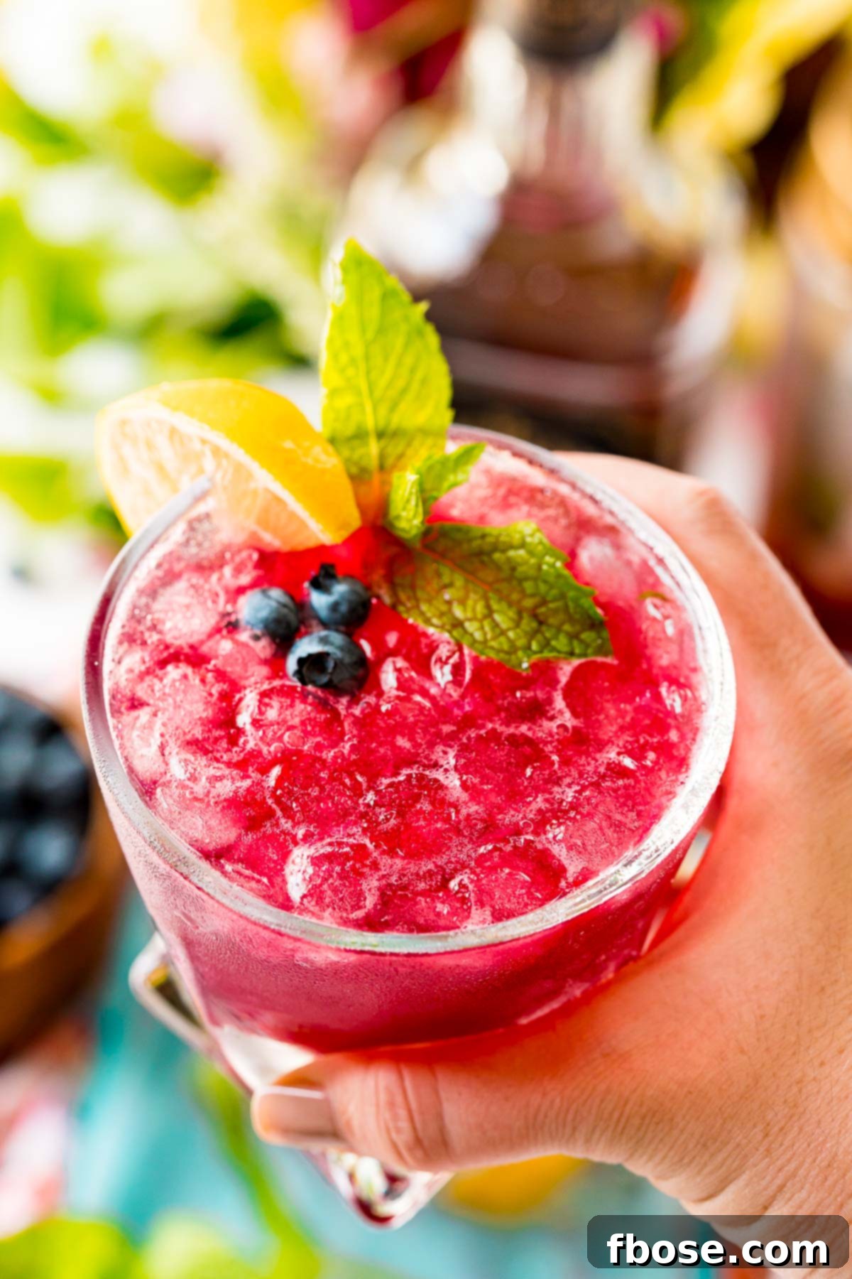Woman's hand holding a blueberry cocktail up to the camera.