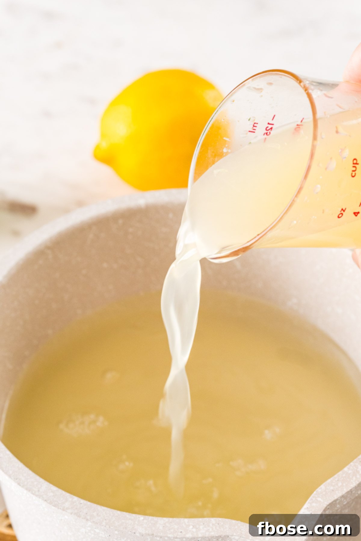 Lemon juice being added to a small pot with water, sugar, and lime juice to make homemade sour mix.