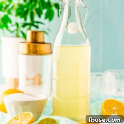 Bottle of homemade sour mix with lemons and limes around it and a cocktail shaker in the background.