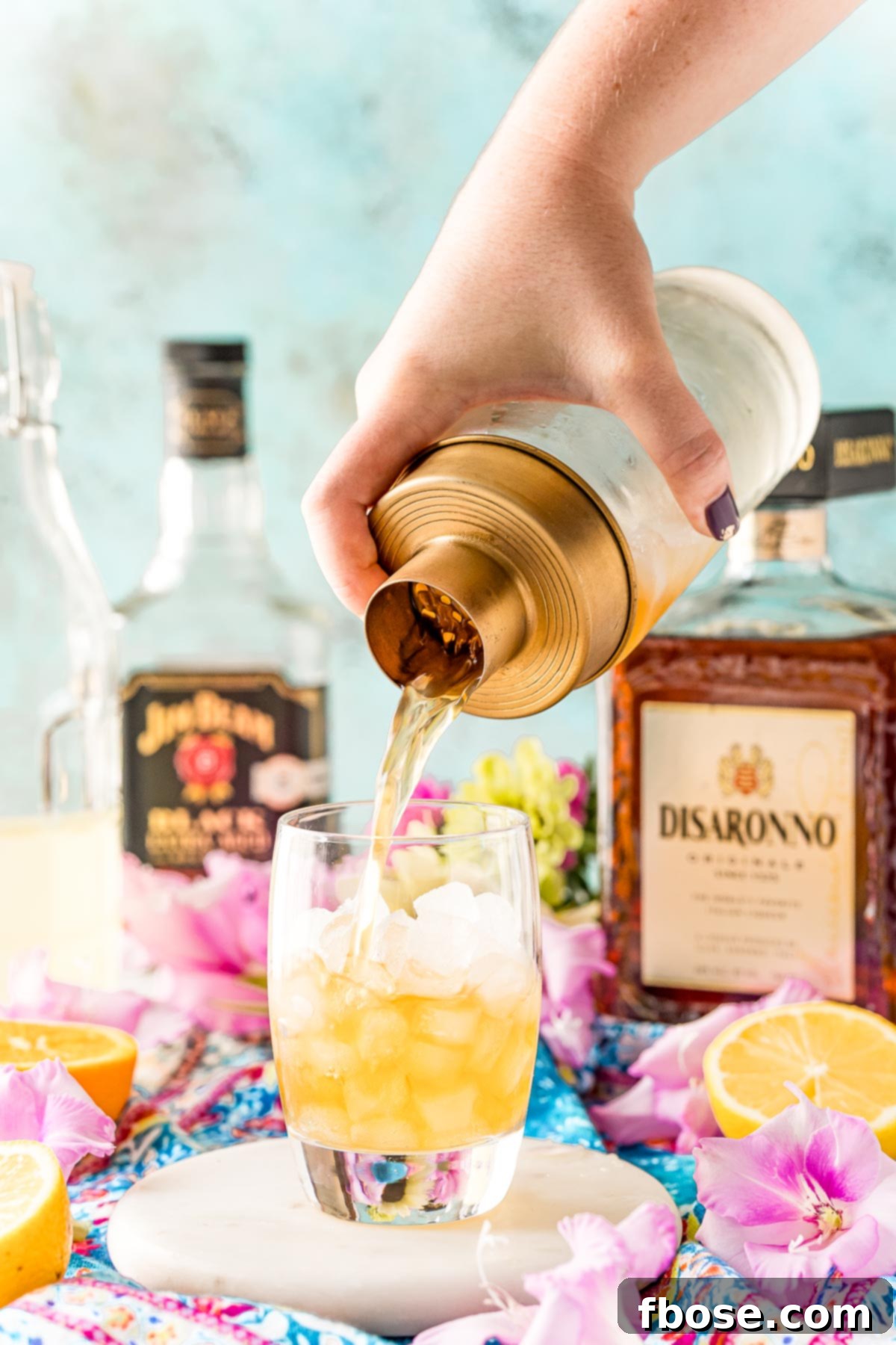 A cocktail shaker pouring a drink into a rocks glass filled with ice.