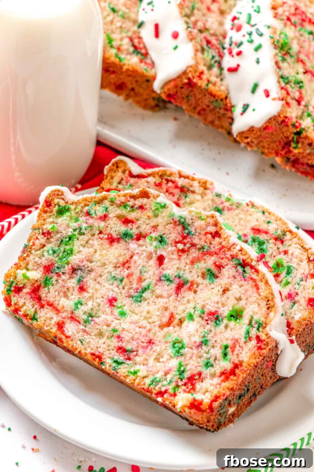Close up photo of two slices of Christmas Funfetti Bread on a white plate, showcasing colorful sprinkles and vanilla glaze.
