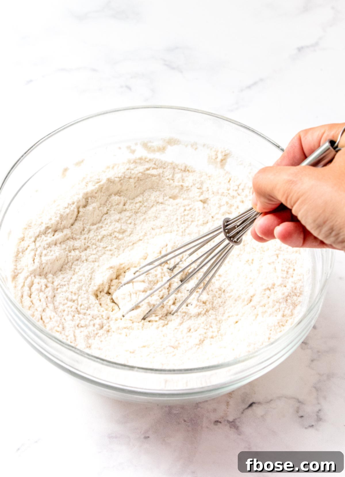 Dry ingredients for quick bread being whisked in a glass mixing bowl, showing flour, baking powder, baking soda, salt, and cinnamon.