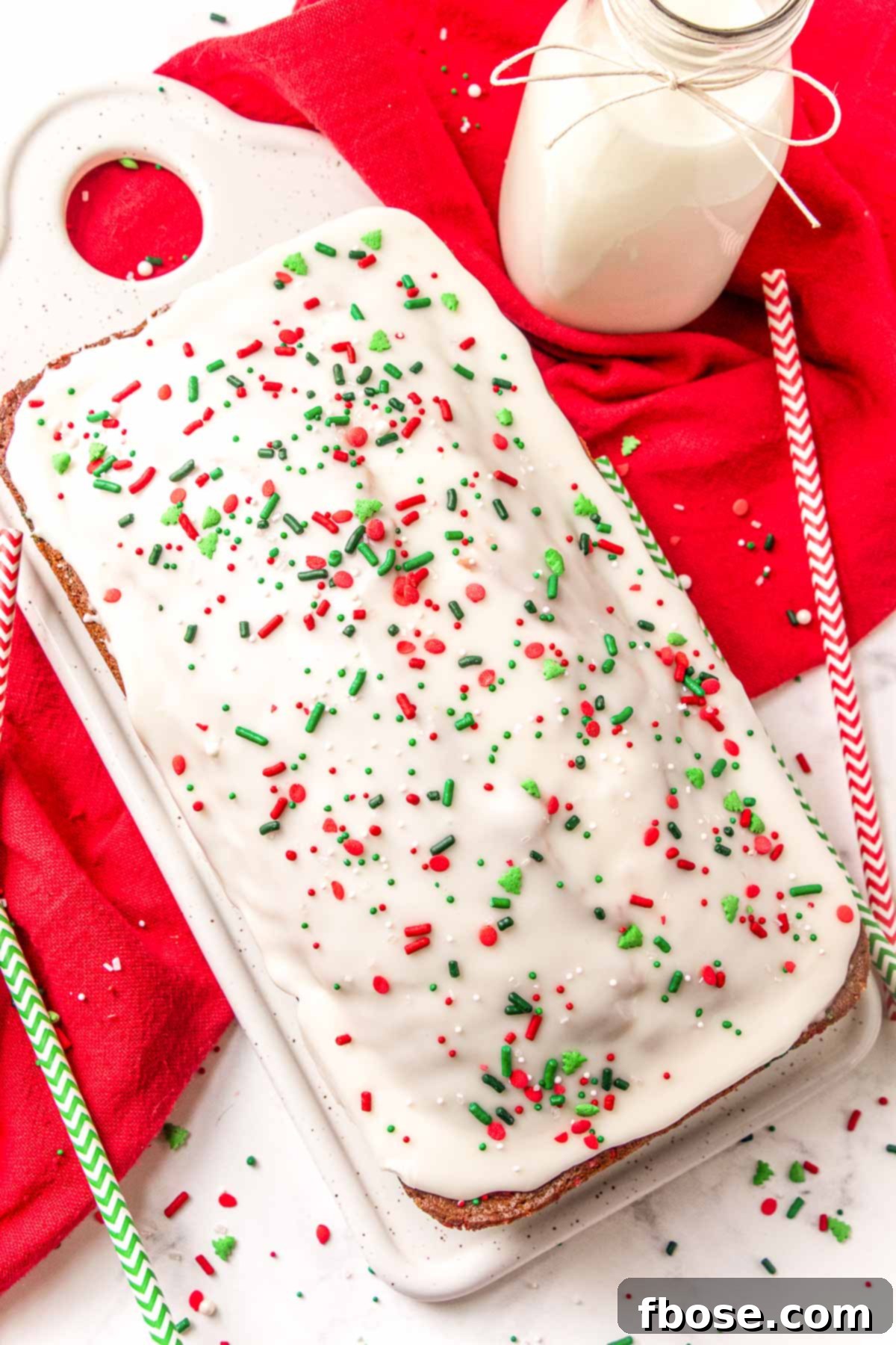 A beautifully glazed loaf of quick bread with Christmas sprinkles on a white serving tray, ready to be sliced.