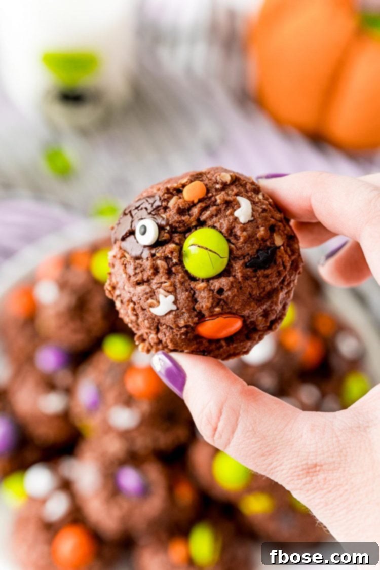 Woman's hand holding a chocolate monster cookie close to the camera.