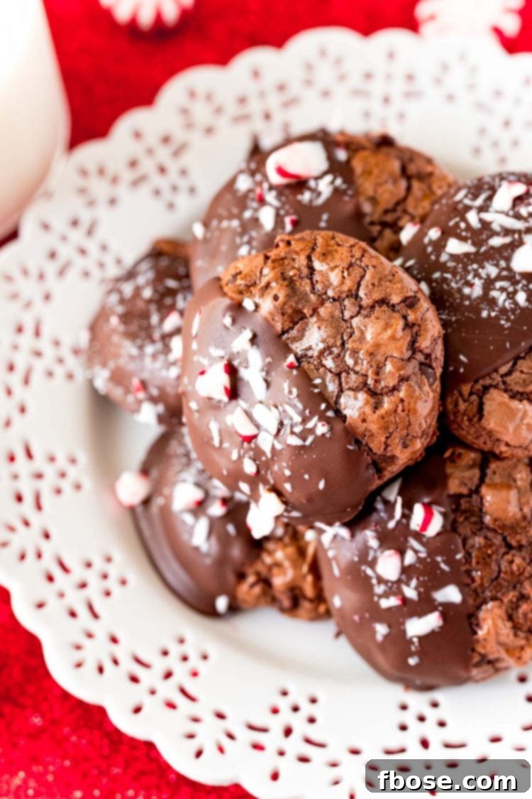 Close up photo of chocolate peppermint cookies on a white plate on a red napkin, showcasing their fudgy texture and festive topping.