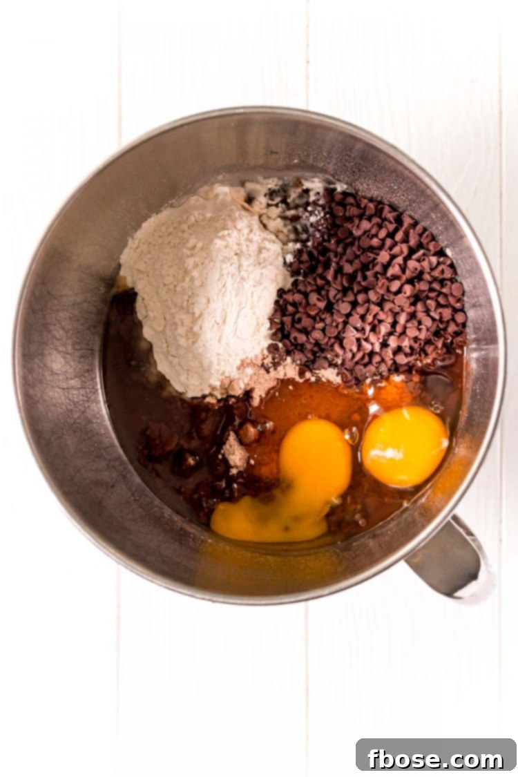 Ingredients to make brownie cookies in a metal mixing bowl, showcasing the rich, sticky batter.