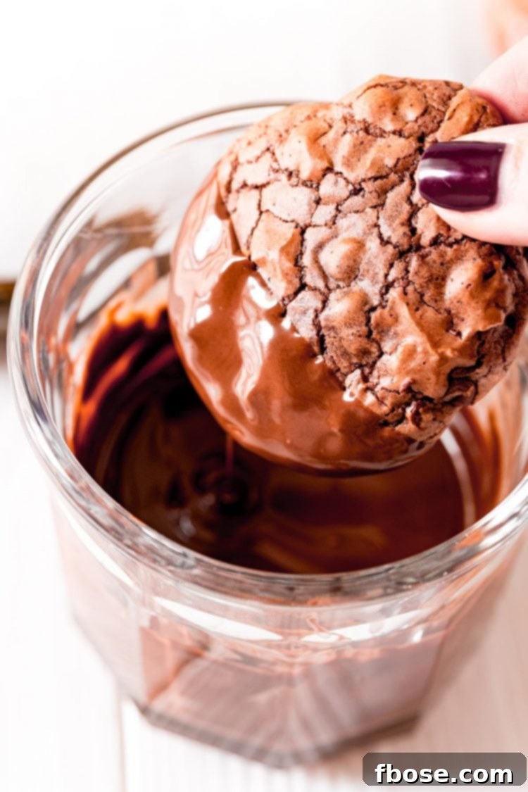 A woman's hand holding a brownie cookie and dipping it in melted chocolate, ready for its festive topping.