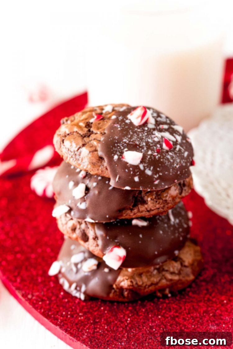 Stack of four peppermint brownie cookies on a red surface, showcasing their height and beautiful topping.