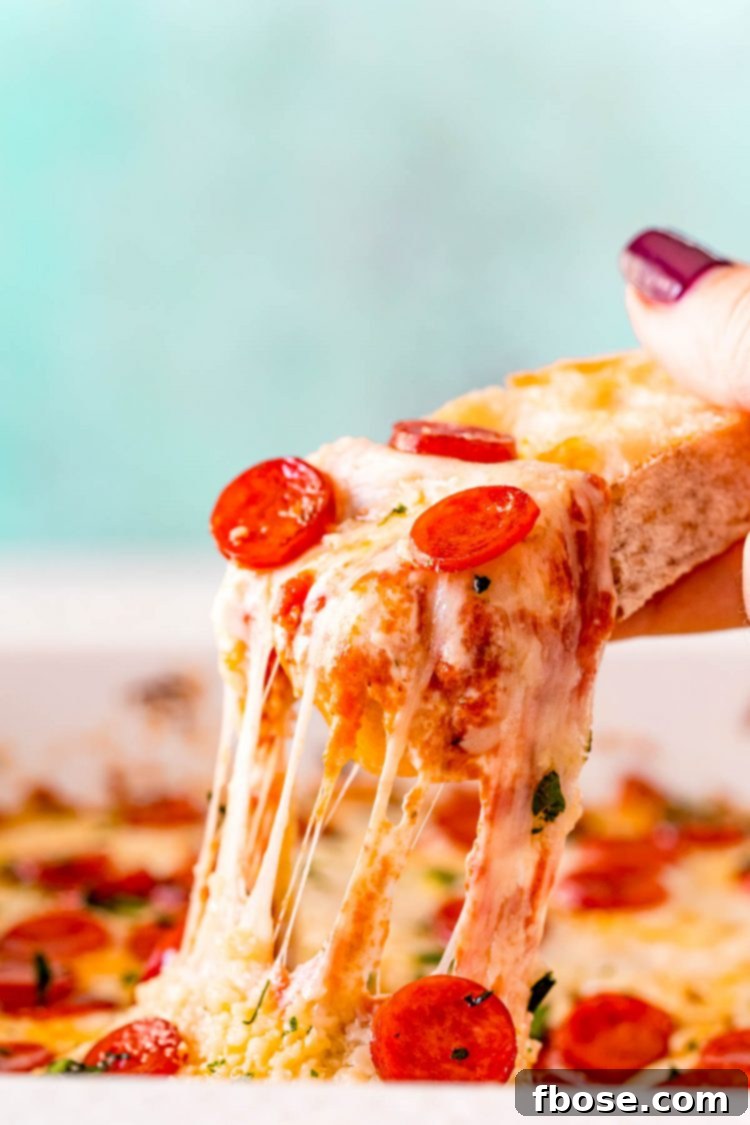 A woman's hand scooping pizza dip our of a white baking dish with a piece of bread.