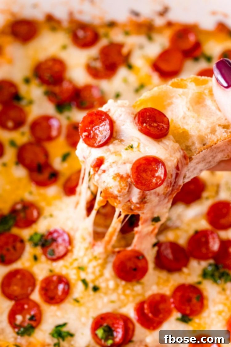 Close up photo of a piece of bread scooping pepperoni pizza dip.