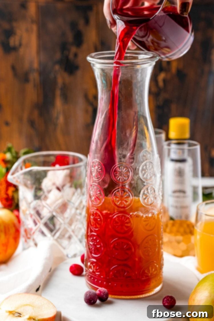Ruby Red Apple Cider Punch 4 Cranberry juice being poured into a large carafe with other juices to make a festive punch.