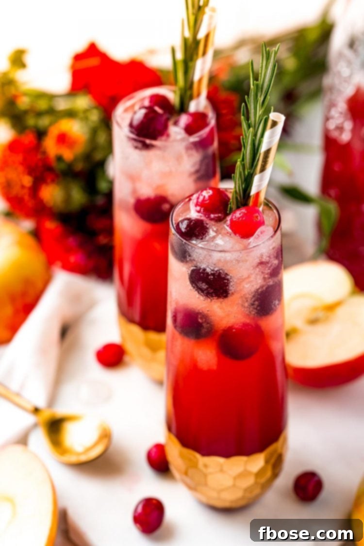 Ruby Red Apple Cider Punch 7 Close up photo of two vibrant red cranberry cider drinks elegantly placed on a white table, surrounded by scattered fresh apples and cranberries, highlighting the festive appeal.