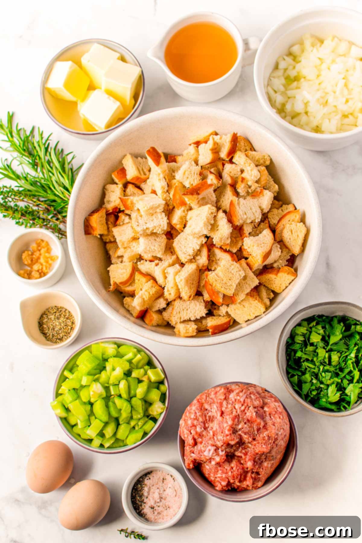 Ultimate Sausage Stuffing 4 Overhead photo of fresh ingredients to make homemade sausage stuffing laid out on a table, including bread, sausage, vegetables, and herbs.