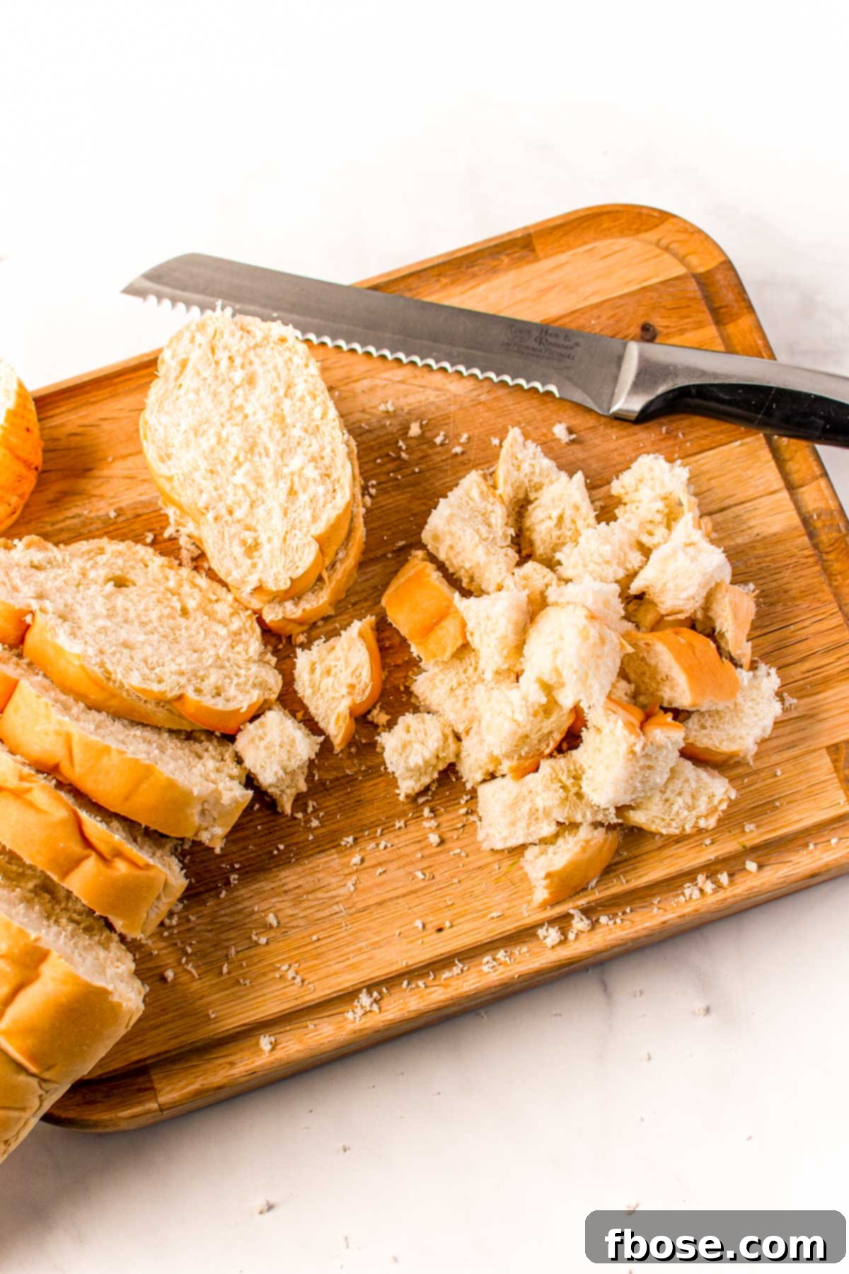 Ultimate Sausage Stuffing 5 French bread being meticulously cut into uniform cubes on a wooden cutting board, preparing it for a delicious stuffing recipe.