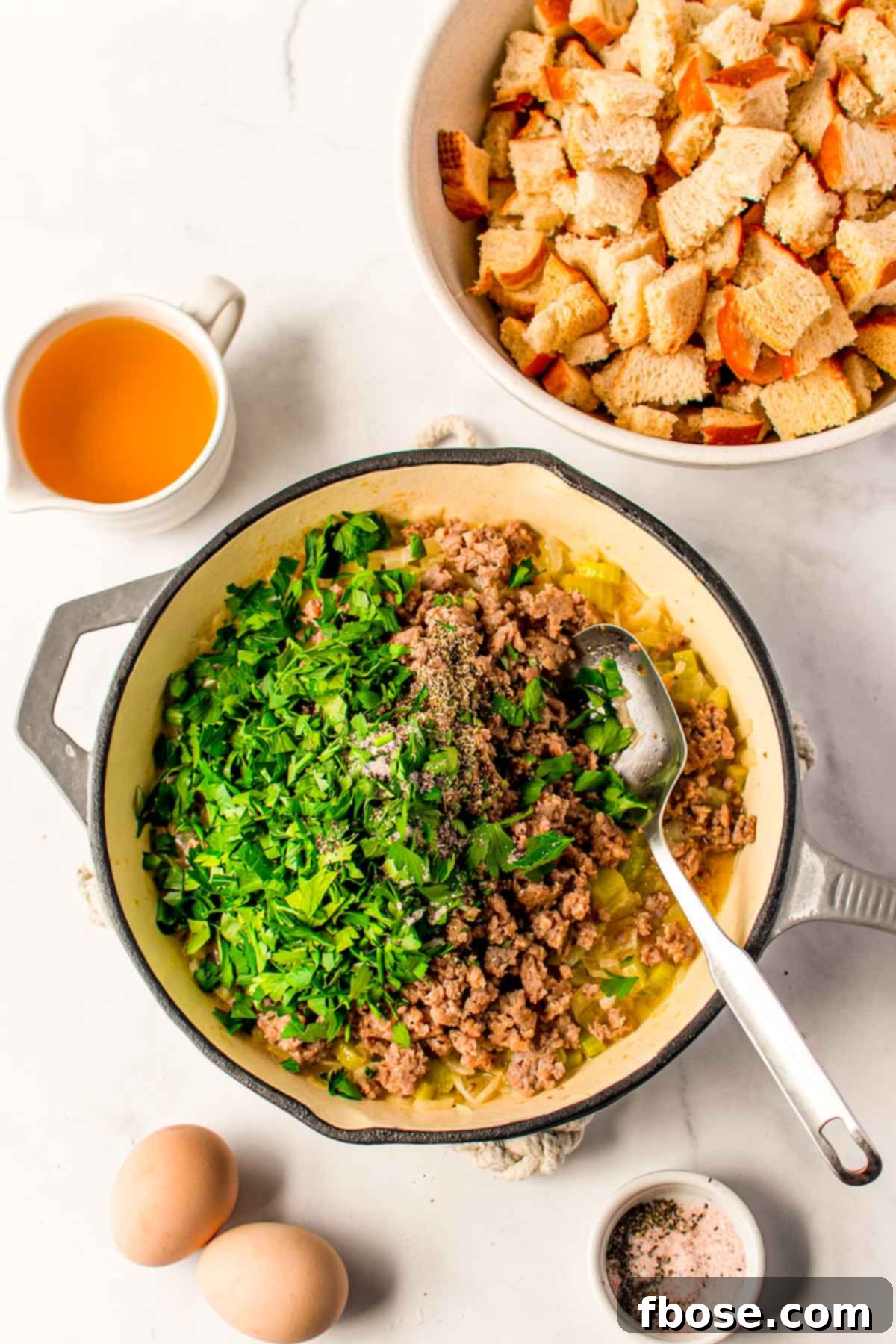 Ultimate Sausage Stuffing 6 Overhead photo of ground sausage and a vibrant mix of fresh herbs being cooked together in a skillet, creating an aromatic base for the stuffing.