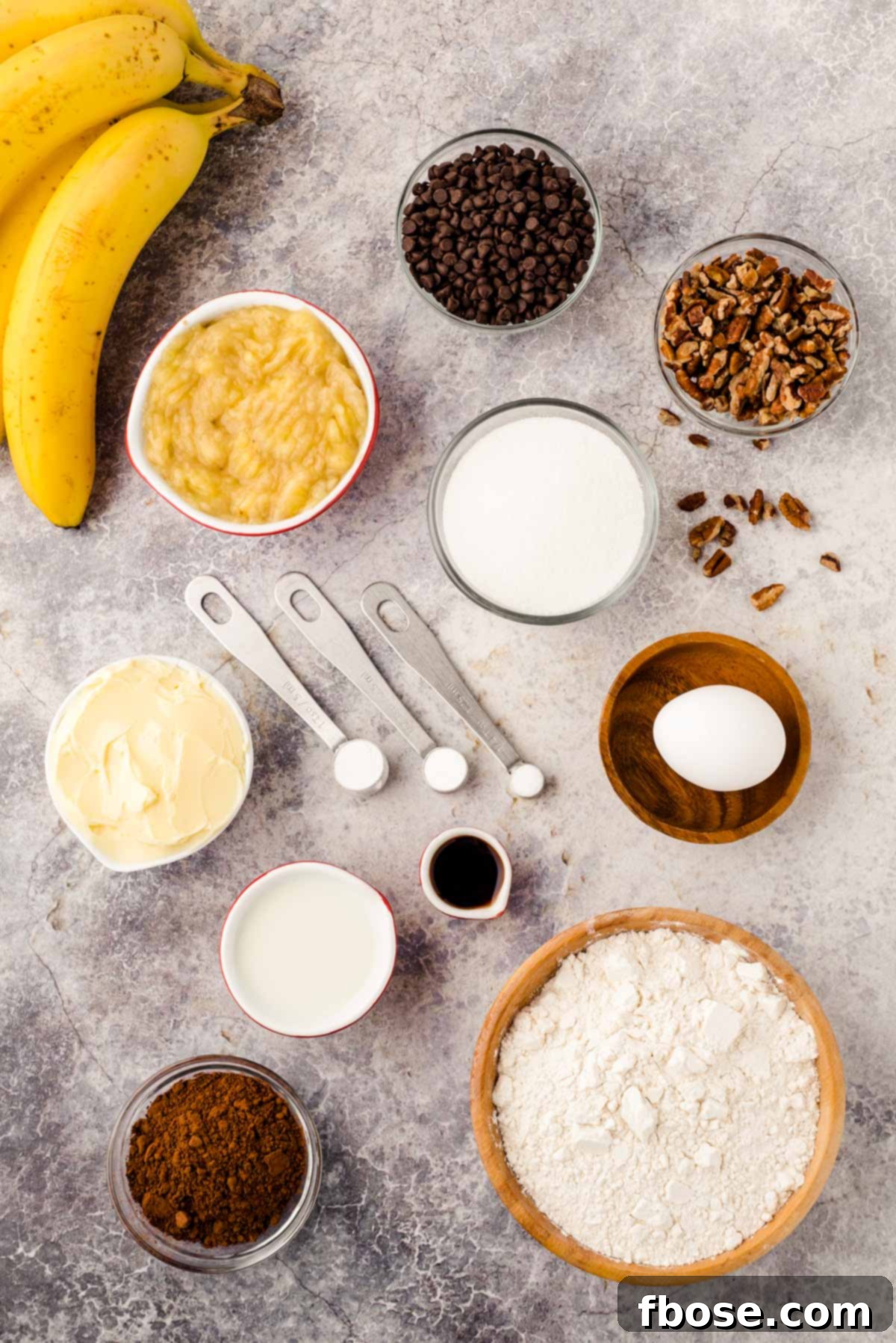 Overhead photo showcasing all the fresh and dry ingredients meticulously laid out on a gray surface, ready to be combined for chocolate banana muffins.