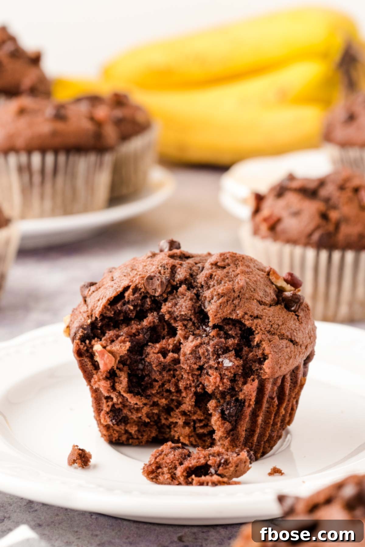 A delicious chocolate banana muffin on a white plate with a bite playfully missing, revealing its moist interior and chocolate chips.