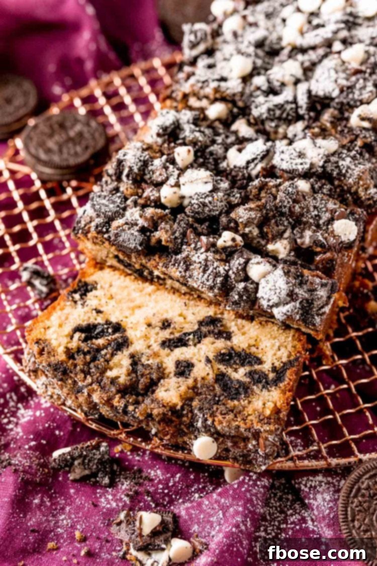 Close up photo of oreo crumb cake on a wire rack partially sliced, highlighting the crunchy crumb topping and moist interior.