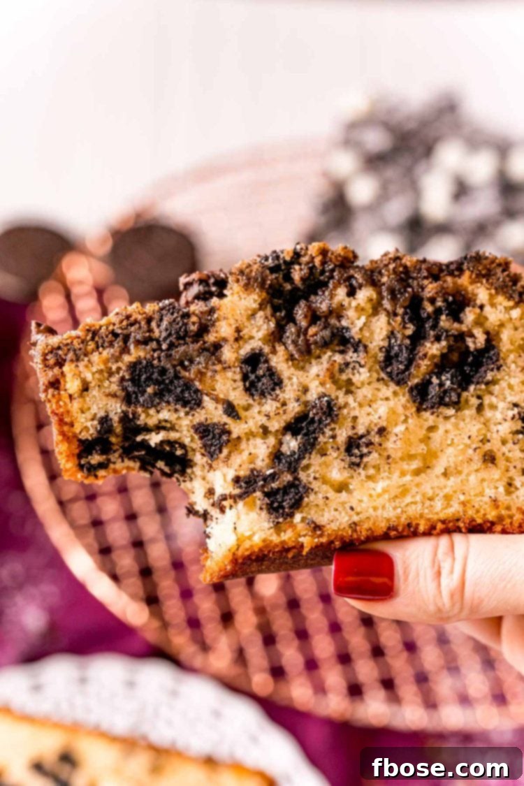 A woman's hand holding a slice of Oreo coffee cake with a bite taken out, showing the rich interior and crunchy topping.