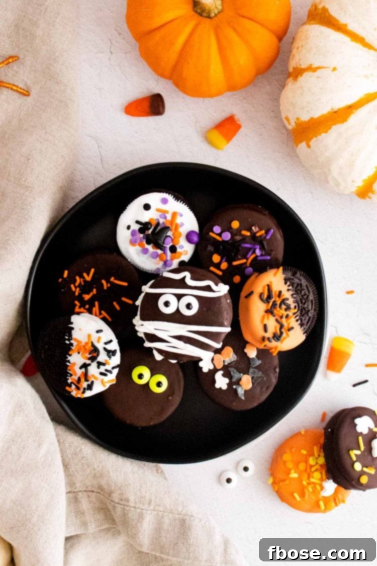 Overhead photo of halloween chocolate covered oreos on a black plate surrounded by pumpkins and candy corn.