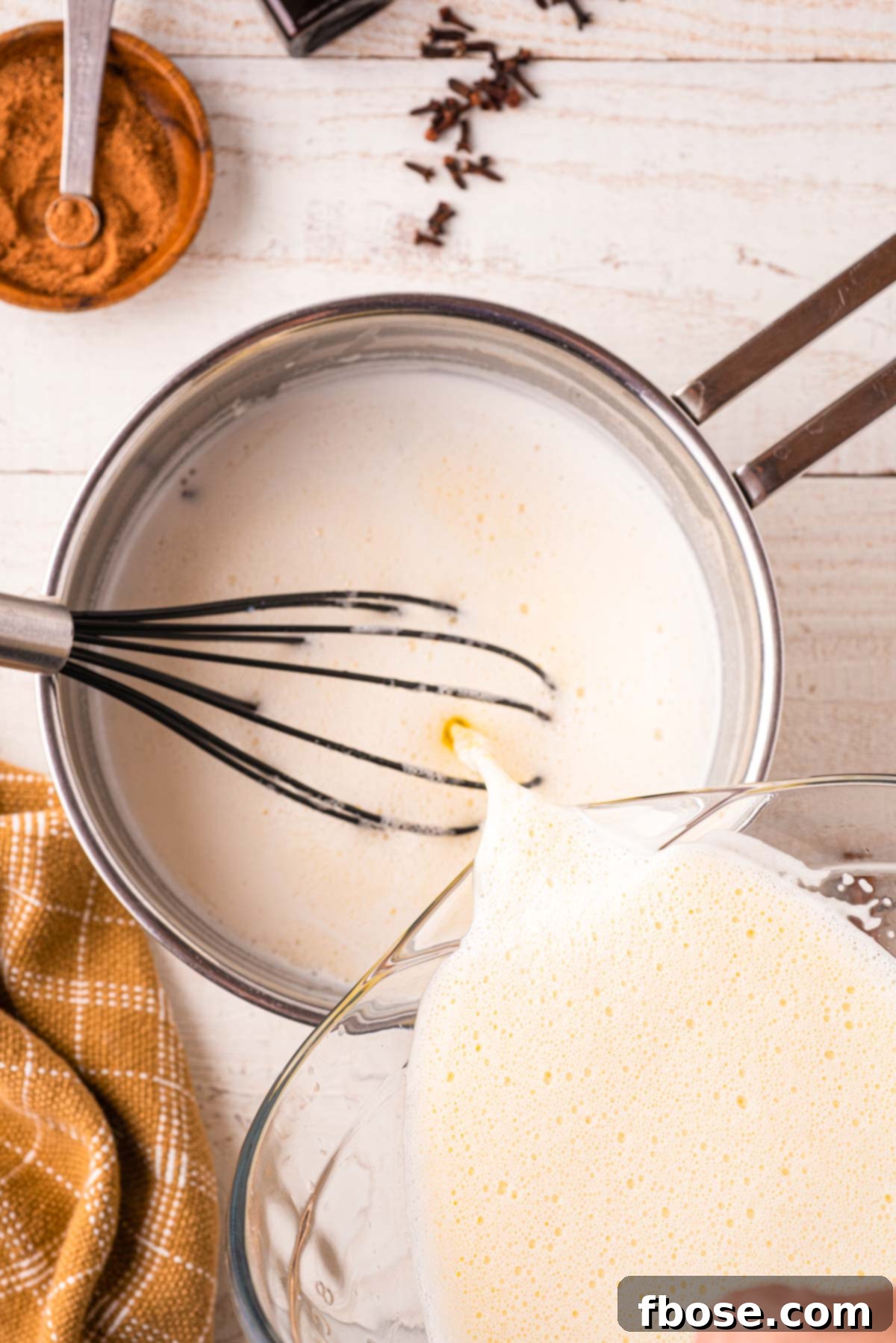 The tempered egg and milk mixture is carefully poured back into the saucepan, joining the remaining spiced milk, ready for final cooking to achieve the perfect eggnog consistency.