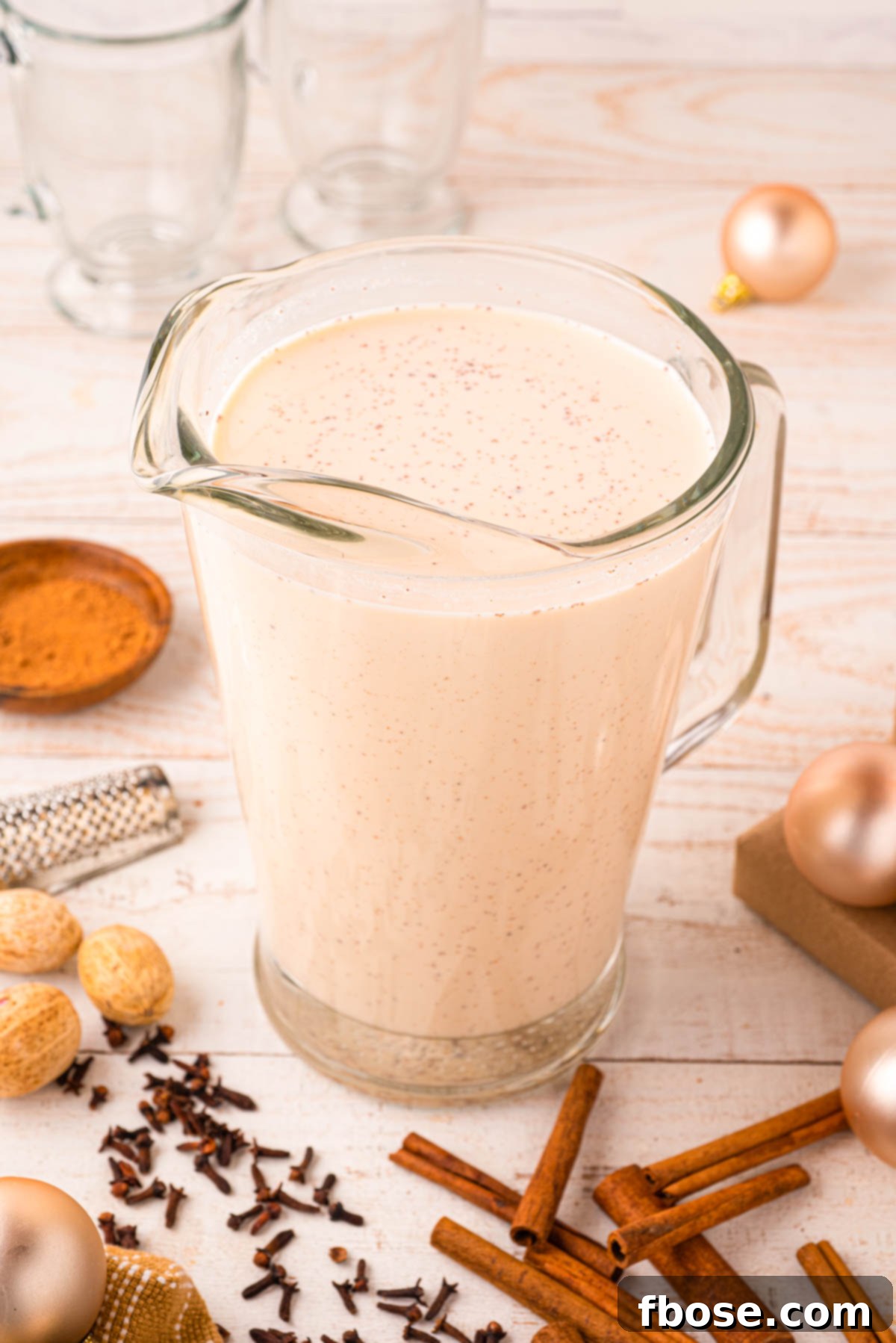 A beautifully presented large glass pitcher, brimming with freshly made, creamy homemade eggnog, ready to be served at a festive gathering.