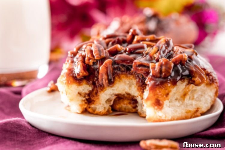 Close up photo of a sticky cinnamon roll on a small white plate with a bite taken out of it, showing its soft interior and gooey topping.