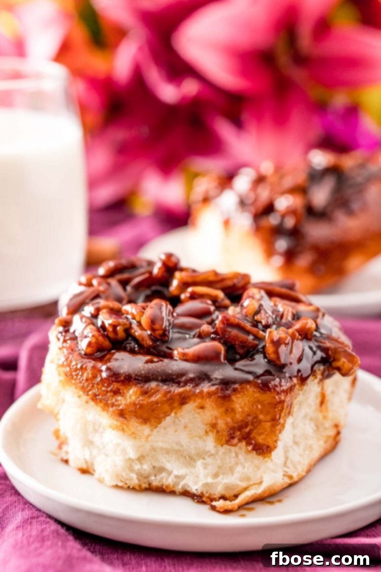 Cinnamon pecan sticky bun on a small white plate with pink flowers and a glass of milk in the background, highlighting a perfect brunch setting.